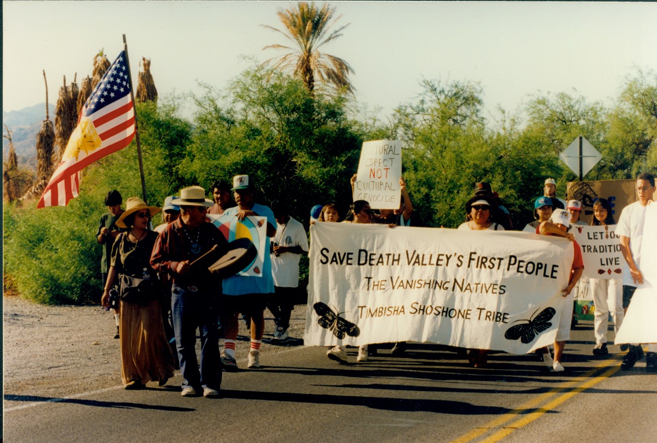 Group marching in street with sign stating "Save Death Valley's First People"