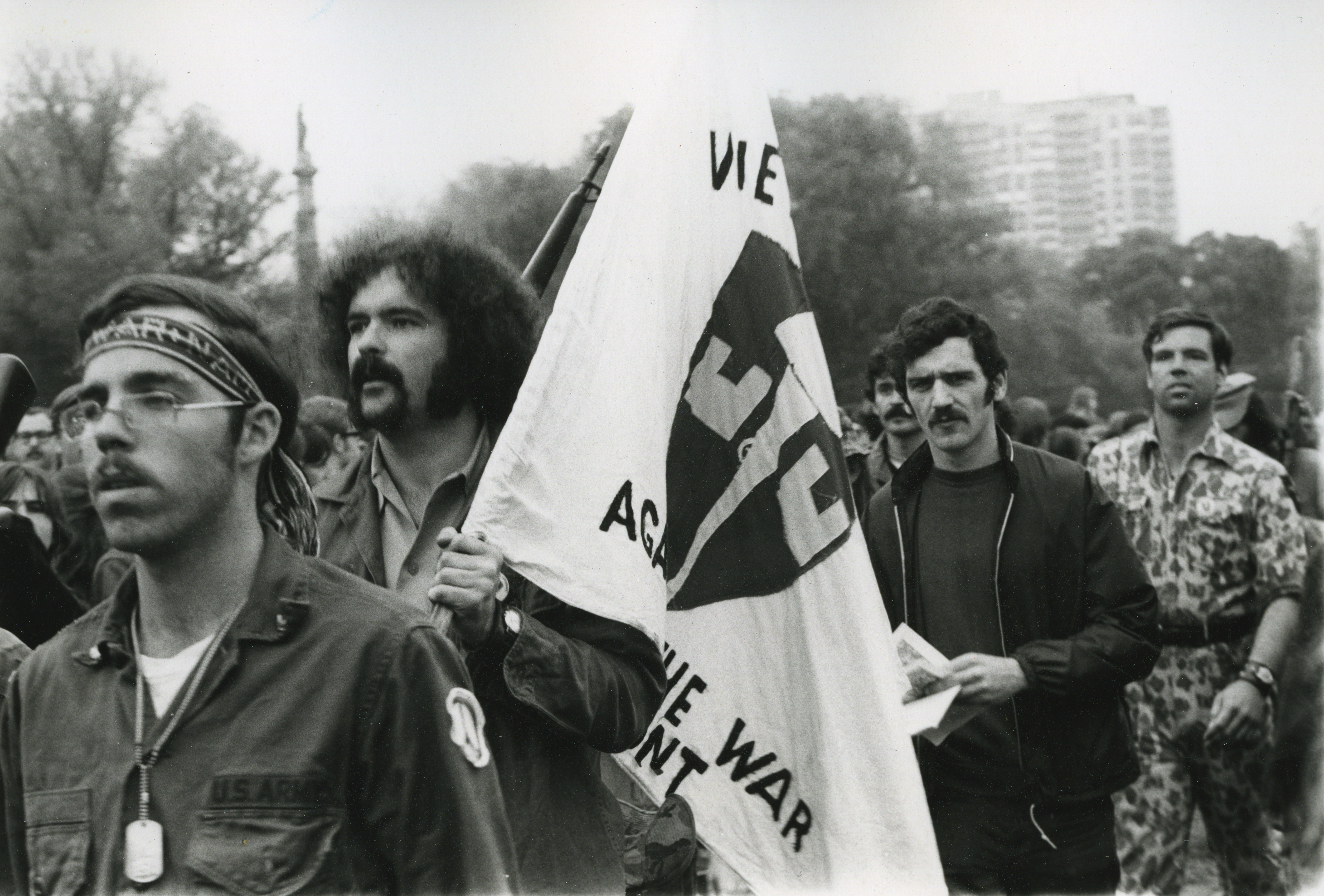 marchers, with close ups of three men, one carrying a Vietnam Veterans Against the War flag