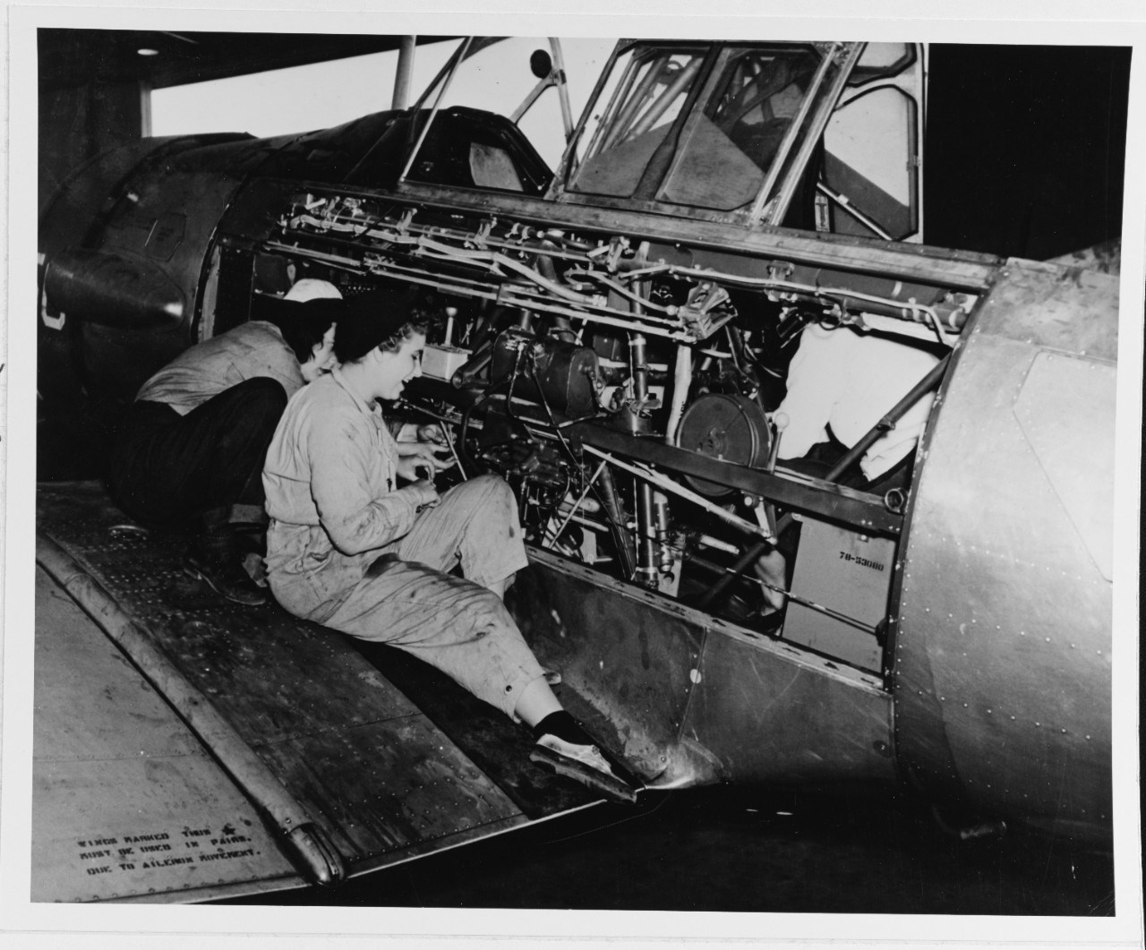 black and white photo of two women in coveralls working on the exposed side of a plane