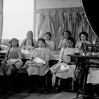 Group of Indigenous girls in uniform pose, sitting at their sewing desks in classroom