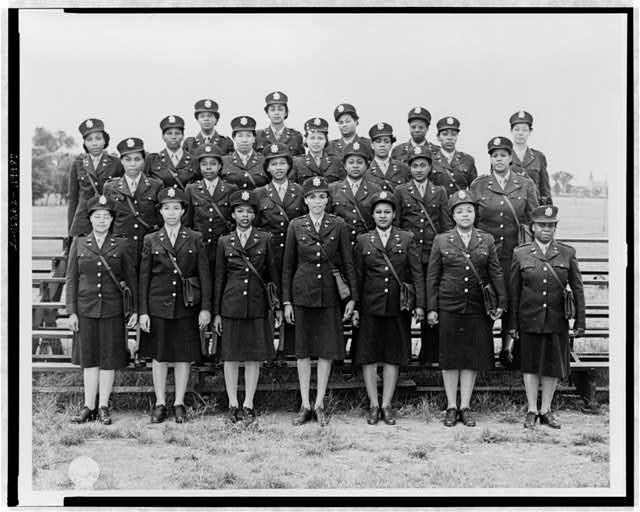 Black and white photo of four rows of Black nurses in dark uniforms and hats with an insignia.