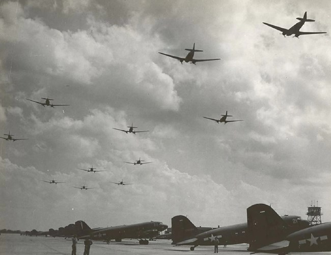 large military prop planes lined up on a tarmac during WW2