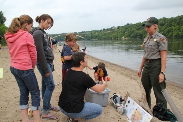 A group of visitors learning about water quality with a Park Ranger at a river's edge.