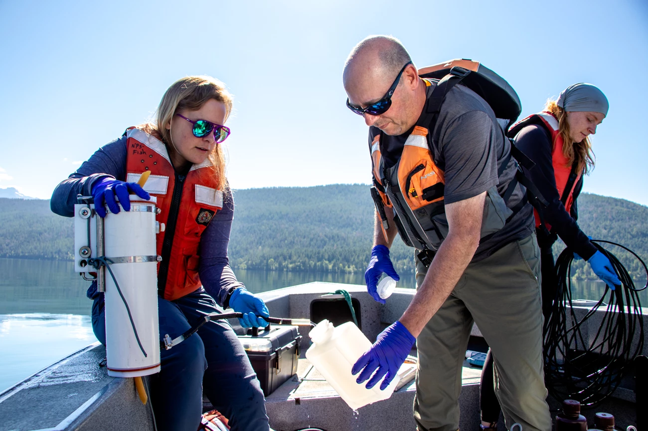 Water Quality Monitoring Three people on a boat hold containers and hoses used to collect water samples and water quality sample measurements.