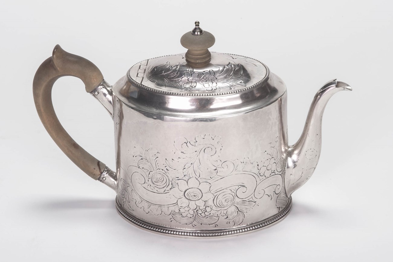 A silver teapot with wood handle.