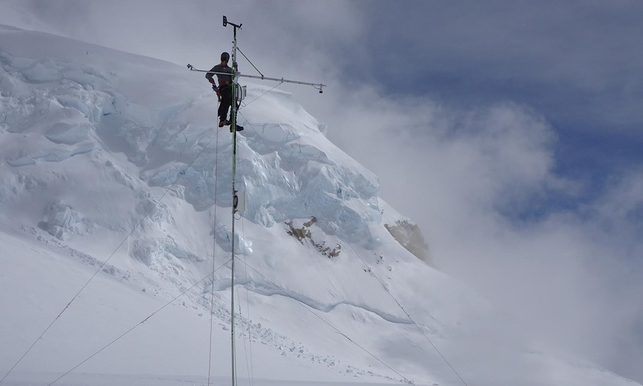 A man high on an antennae on top of a snowy mountain.