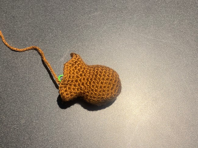 A partially crocheted Beaver Head, light tan with green stitch marker.