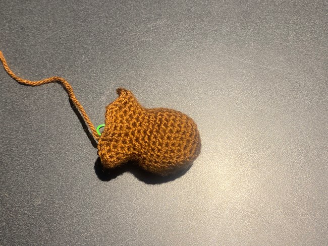 Partially completed crocheted beaver head. A partially crocheted Beaver Head, light tan with green stitch marker.