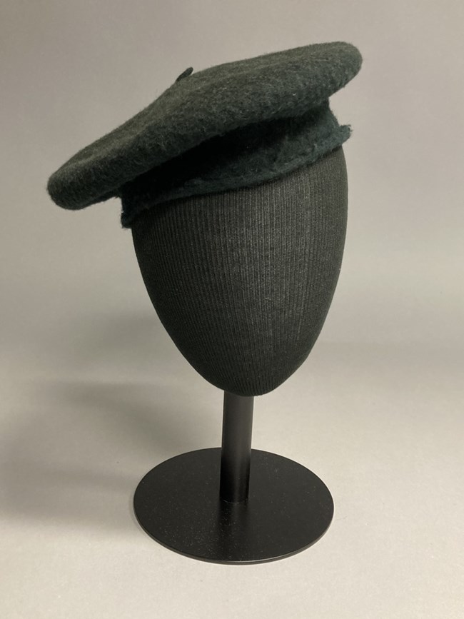 Dark green beret on a black mannequin head.
