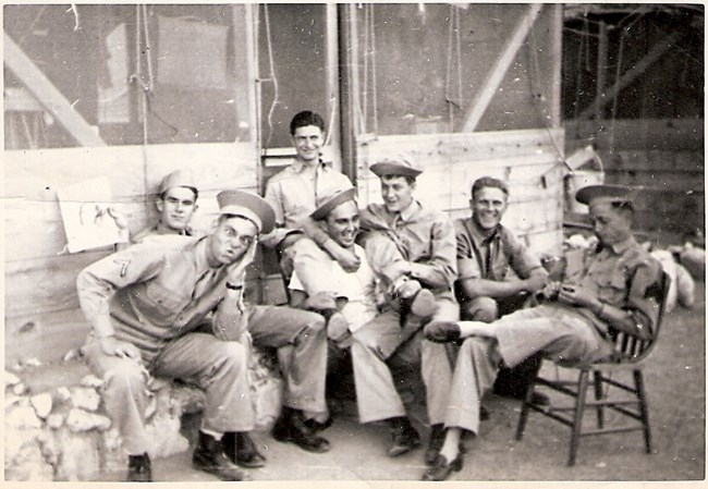 Servicemen Relaxing in Dutch Harbor Group of six men, seated, in uniform, outside wooden building.