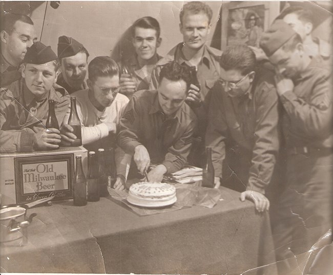 Men crowd around a man cutting a birthday cake