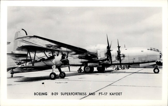 Black and white photo of two planes, smaller with a propeller in the front. Larger one behind with wing propellers.