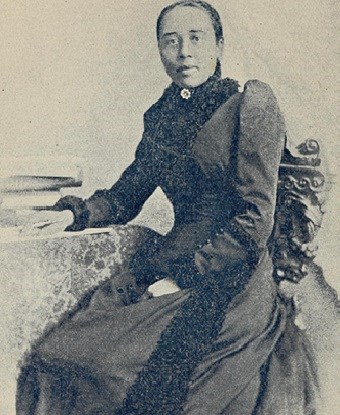 Anna J Cooper A woman sits in a decorative chair with a long sleeved and high necked dress