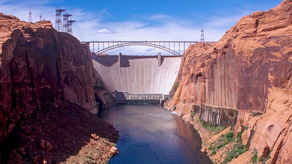 a river flowing between two cliffs below a concrete dam with a height of 710 feet, and a crest length of 1,560 feet