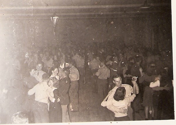 Men and women dancing together in large hall.