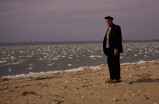 Freeman Tilden stands on a beach at the edge of the water in a suit
