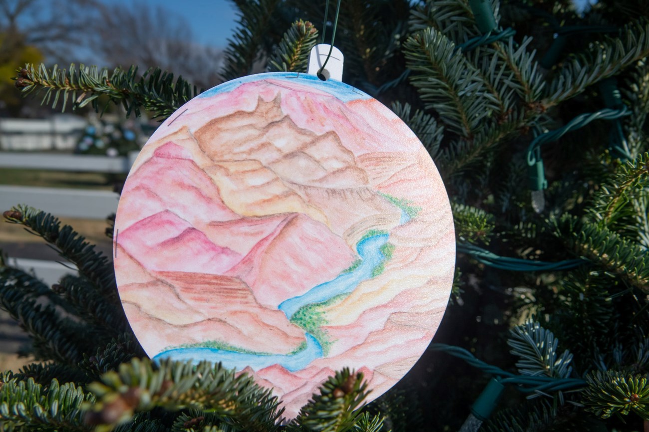 ornament with a drawing of red canyons portaying the grand canyon national park. The ornament is hanging from christmas tree