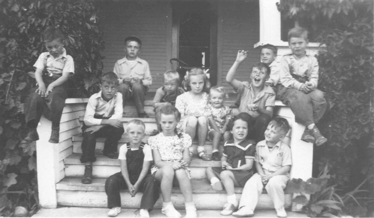 Black and white photo of a group of children sitting on steps to a house with different facial expressions