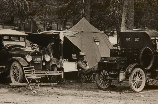 Two old style cars in front of a camping set up