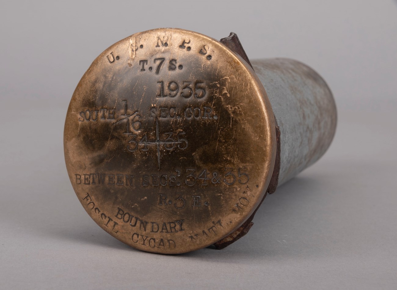 Round bronze marker cap NPS and Fossil Cycad National Monument and 1935 date.