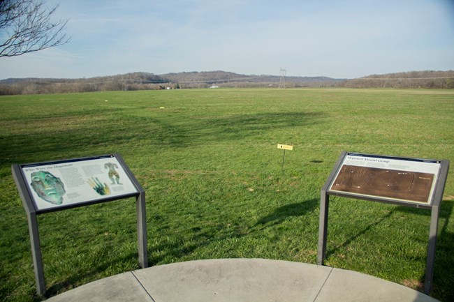 two large descriptive signs lead visitors into a wide grassy field.