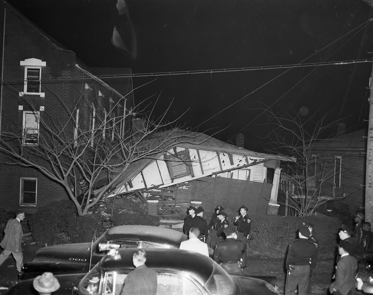 A black and white photo of police officers standing in front of a collapsed house