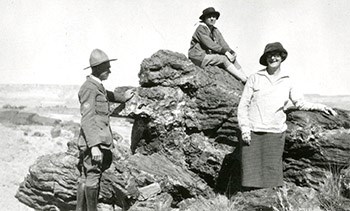 Two adults one man one woman lean on large rocks as a child sits atop the rocks behind them.