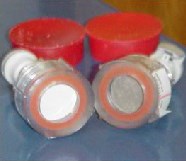 IMPROVE particle filters Two air filters side by side. They both appear as tubes made of white and translucent plastic covered by fiber at the end. The fiber on the left tube is white and new, the tube on the left is used and tinted gray.