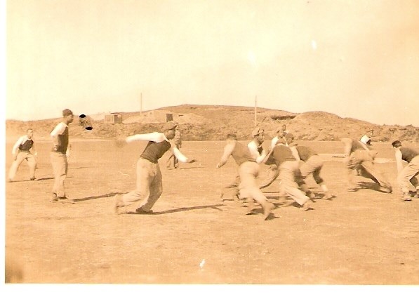 sepia toned photo of African American and white men playing football on a dusty field.