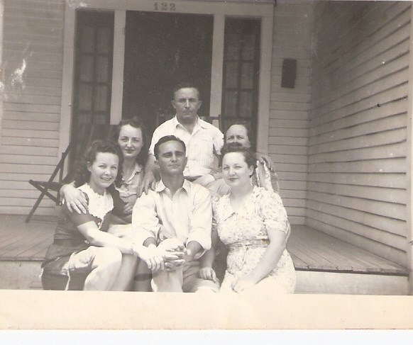 Family of six seated for casual portrait on house porch.