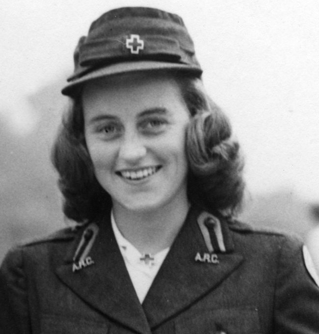 Kathleen in Red Cross uniform A black and white photo of a smiling young woman from the shoulders up, in a blazer with pins spelling “ARC” on each lapel, a cap with a metal pin in the shape of a medical cross, and the same pin on her collar. Her hair is curled in waves.