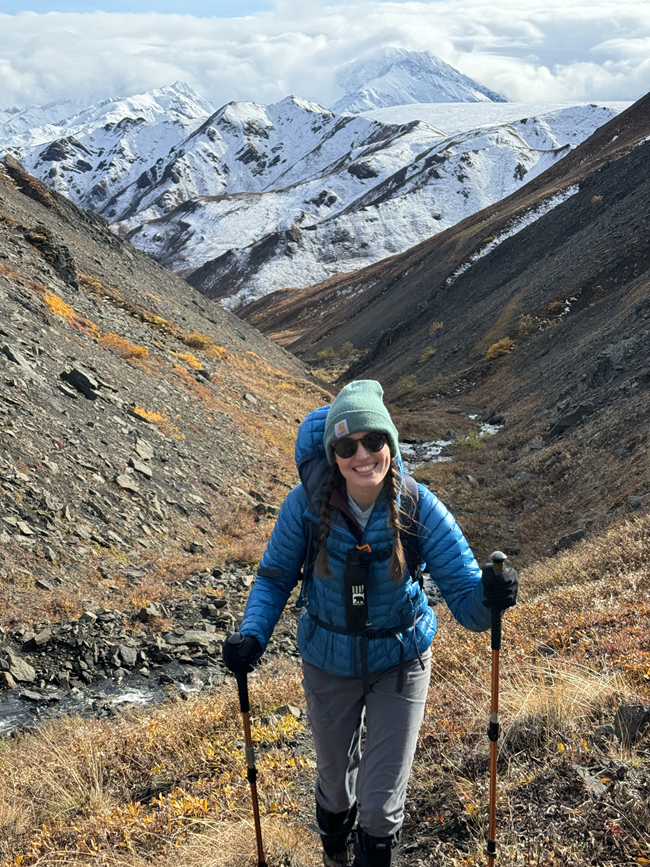 Laura Vachula A woman hiking with snowy mountains behind her.