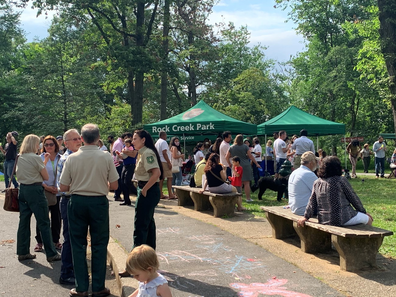 lt= People mingle in a grassy area near pop up tents with the NPS logo