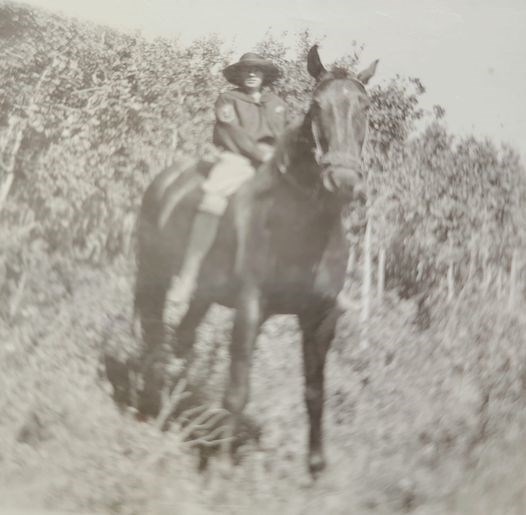 Mae Burns on horseback wearing breeches, shirt, and hat.