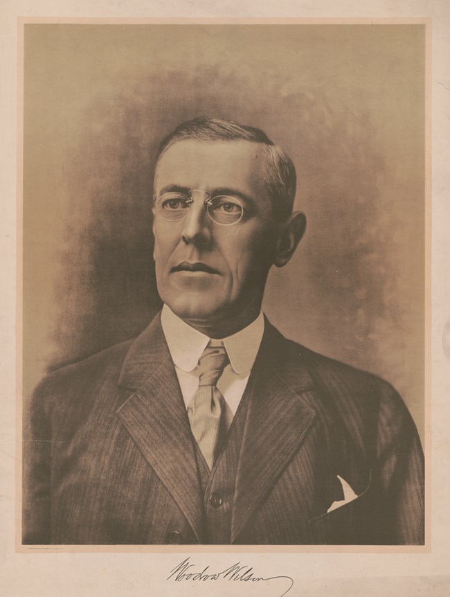 Illustration of a white man wearing glasses and a suit. Under the man is the signature of Woodrow Wilson