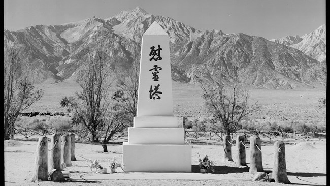 A white obelisk with Japanese characters with mountains in the background