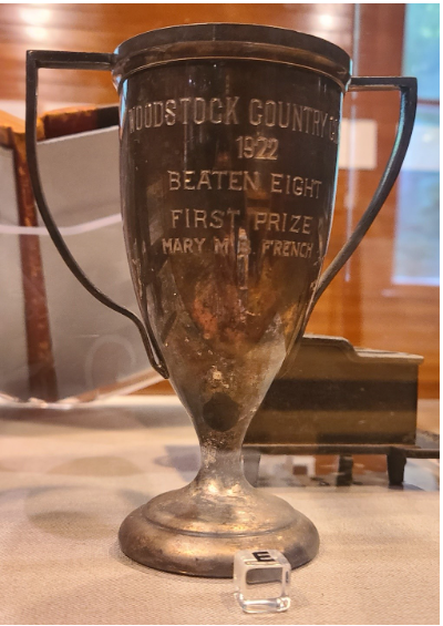 One gold trophy with bell like body, two angular handles, and a circular base. On the body is inscribed “Woodstock Country Club / 1922 / Beaten Eight / First Prize / Mary M.B. French”