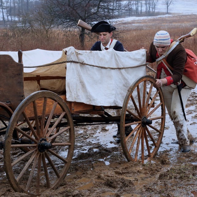 outdoors, mud, wagon, two men pushing