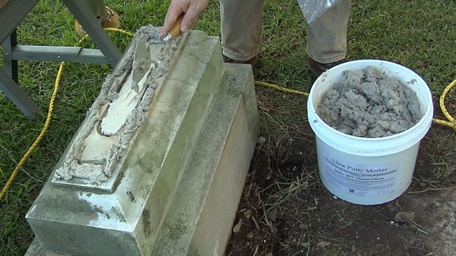 For this reset we are going to use a two part epoxy on the broken tab and a lime pointing mortar around the edge of the headstone. Care should be taken when mixing a two part epoxy. Jason Church applies new mortar to the cleaned base of a headstone.