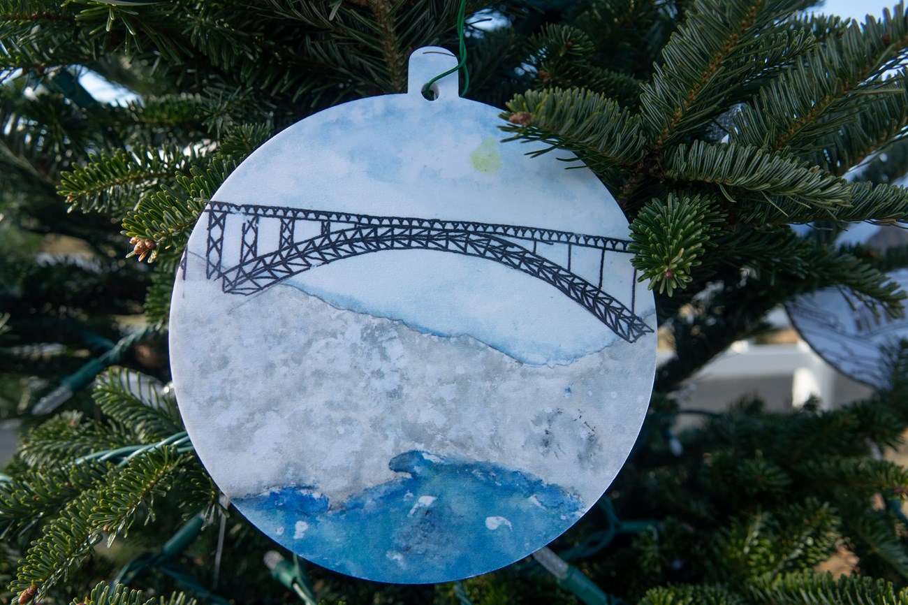 ornament with drawing of a bridge. Ornament is hanging from chritmas tree