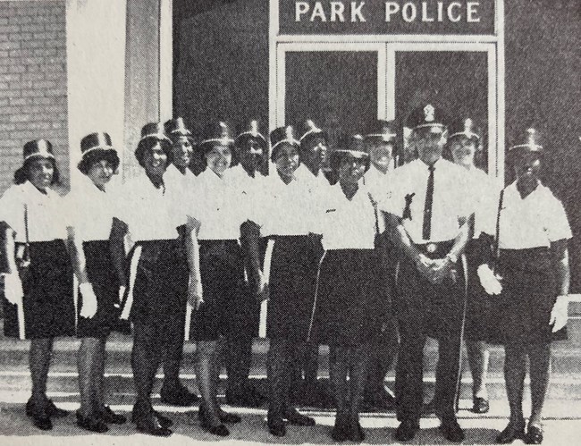 Group of women with two men in US Park Police uniforms stand posing outside the police station.