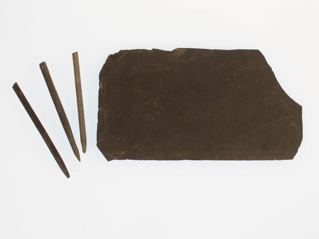 a large slate and three pencils arranged on a white background