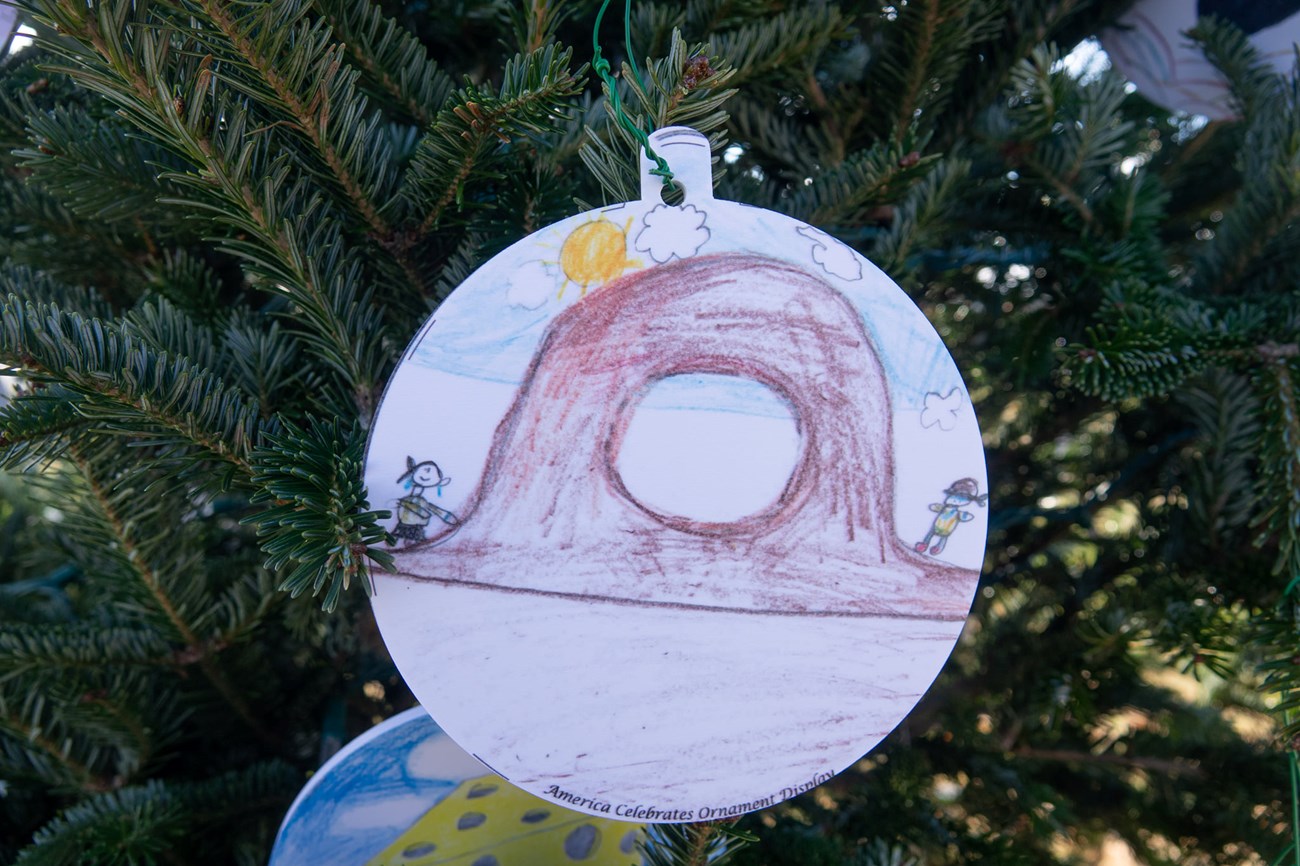 ornament with drawing of the arch at rainbow bridge national park. The ornament is hanging from christmas tree