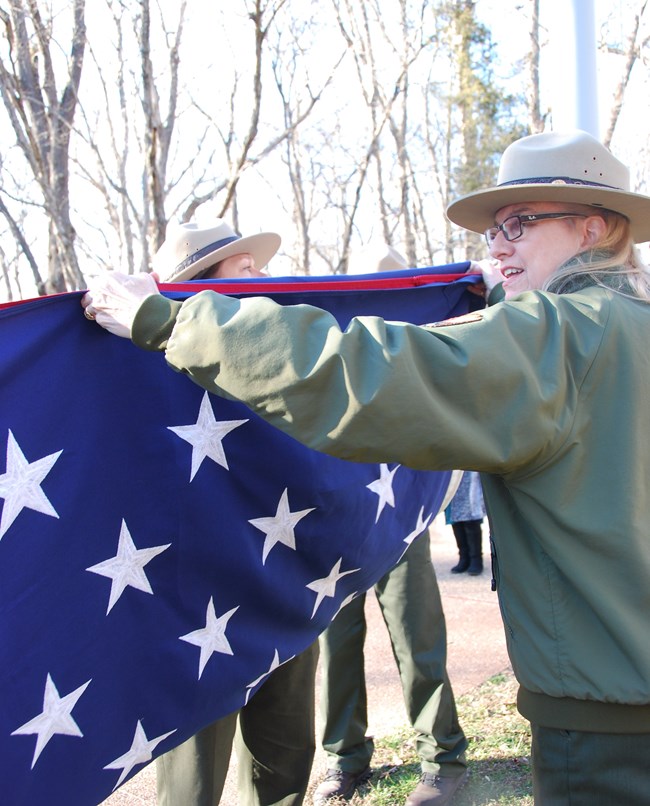 Park ranger folding American flag with blue field showing.