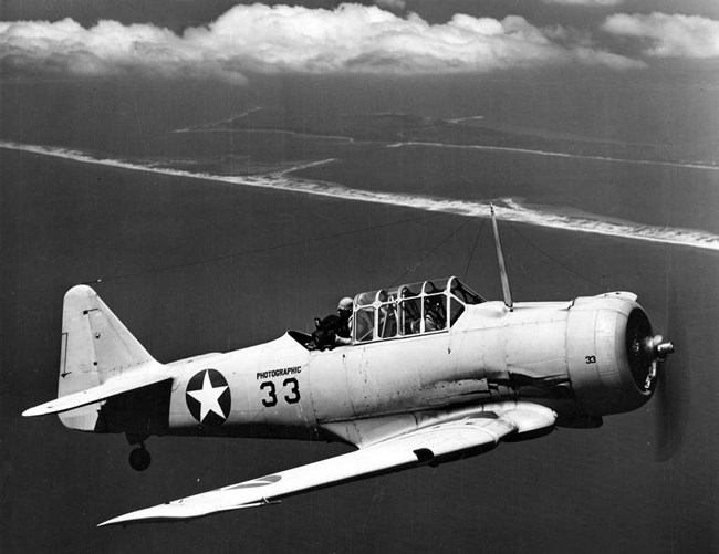 Black and white photo of a propeller plane in front of a visible coastline