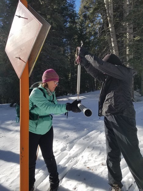 Two researchers weighing a tube filled with snow to figure out water content.