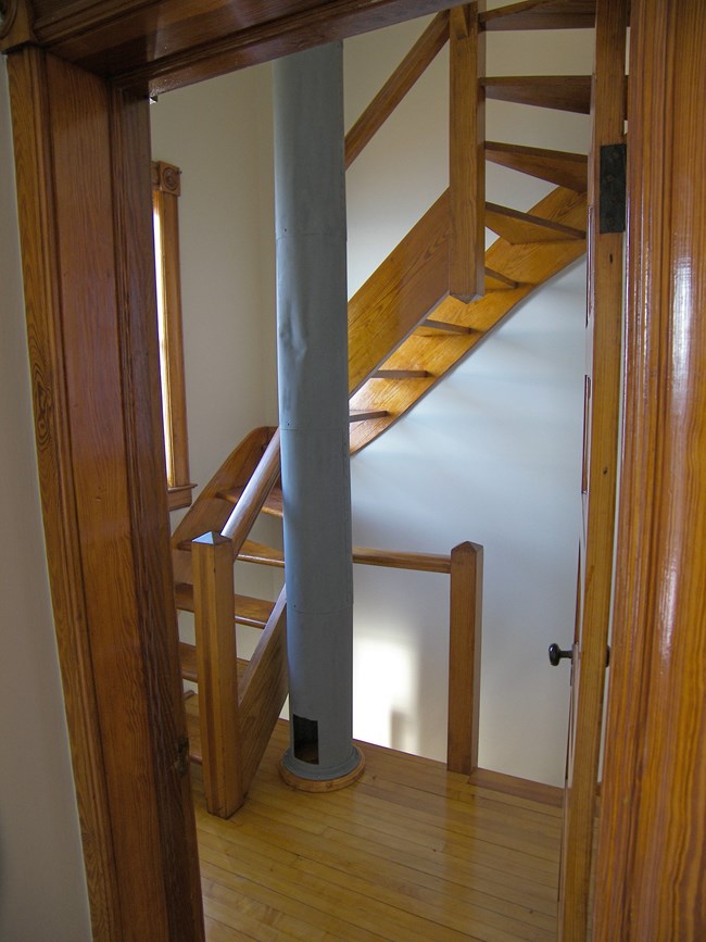 A door open to a wooden staircase and grey tube in the center.