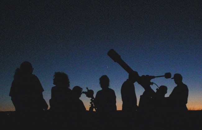 Silhouettes of people with telescope in front of dark blue sky