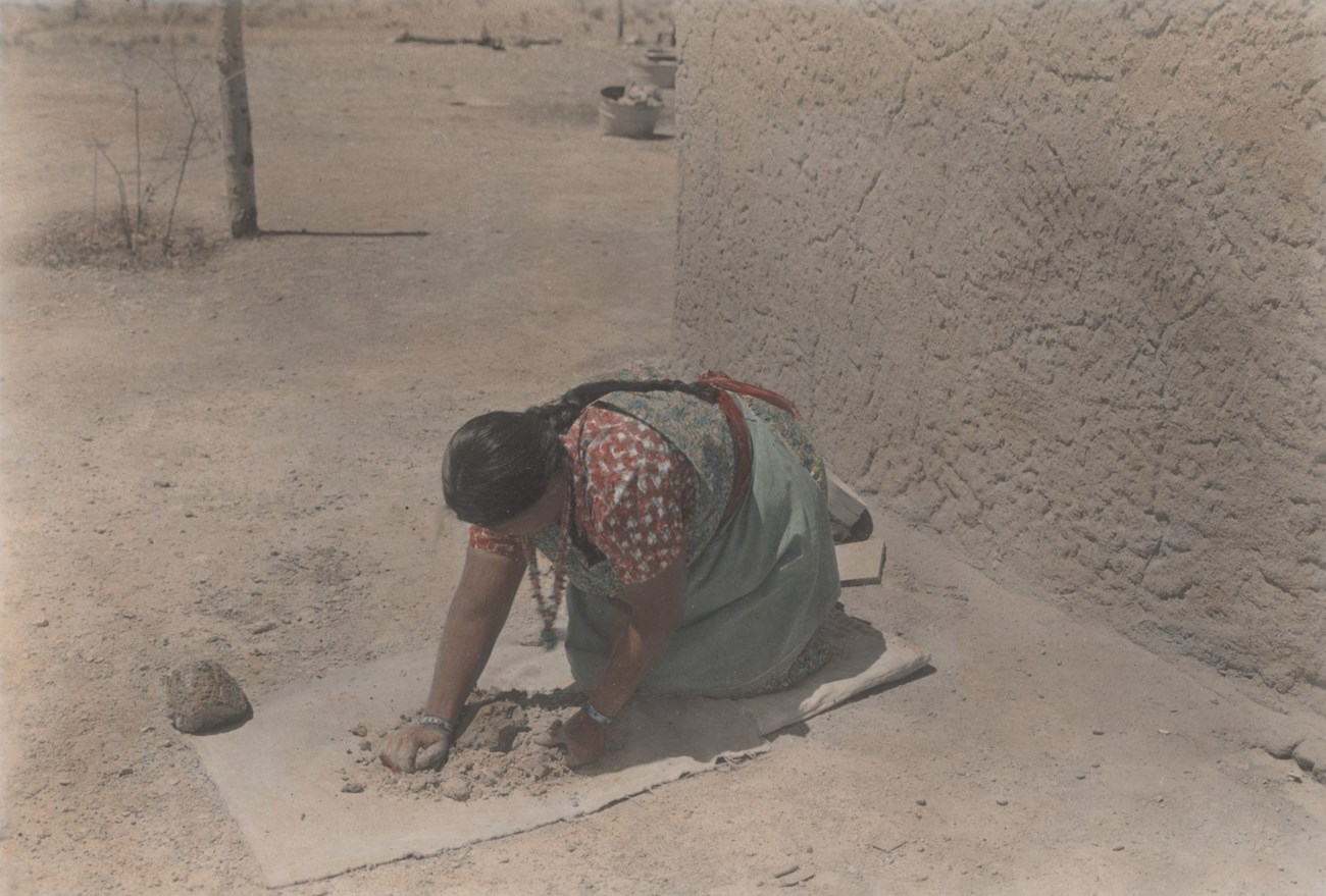 Legoria Tafoya kneels on the ground kneading clay