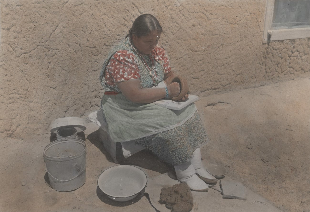 Legoria Tafoya sits iin a chair working clay into the base of a pot.